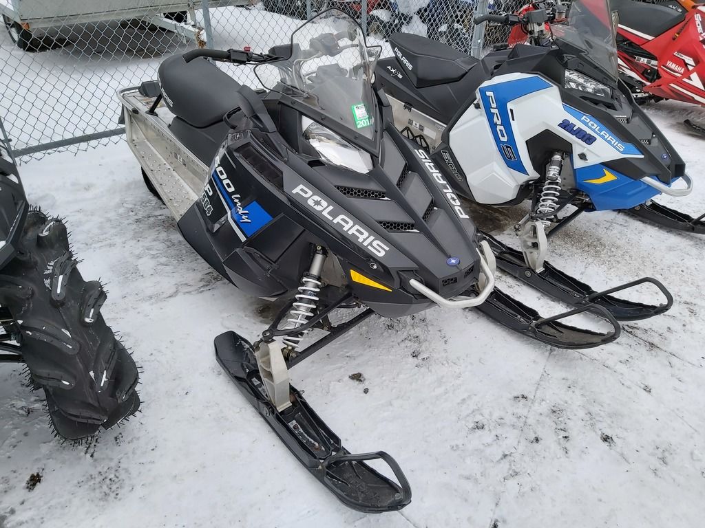 Black Polaris INDY® 600 snowmobile parked on the snow next to a fence and other snowmobiles.